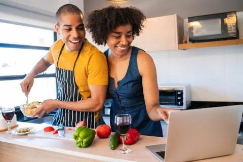 Latin couple using laptop while cooking in kitchen. Stock Photos