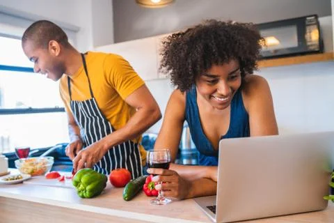Latin couple using laptop while cooking in kitchen. Stock Photos
