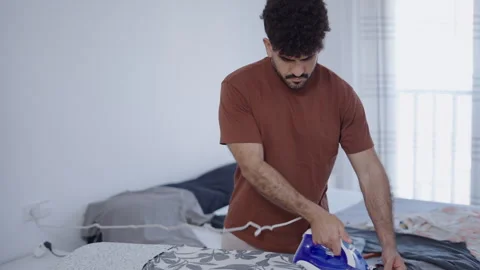 Latin guy ironing his printed shirt in his room Stock Footage 257586502