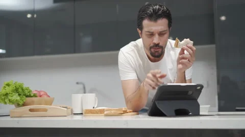 Latin handsome man eating bread with tuna and looking digital tablet for foll Stock Footage 168620777