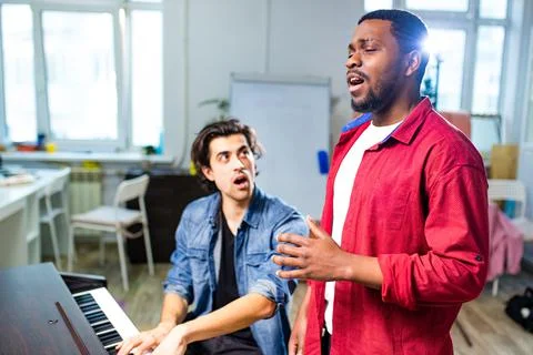 Latin hispanic man learning to play on piano with caucasian teacher in classroom Stock Photos
