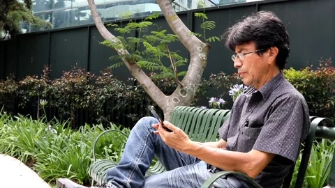 Latin hispanic middle aged man using his cellphone while sitting on a park bench Stock Footage 199530671