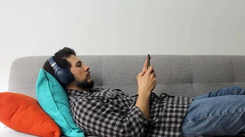 A latin man with beard lying on a couch typing on his smartphone Stock Footage 340583411