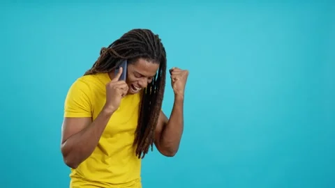 Latin man with dreadlocks celebrating while talking to the mobile Stock Footage 241189618