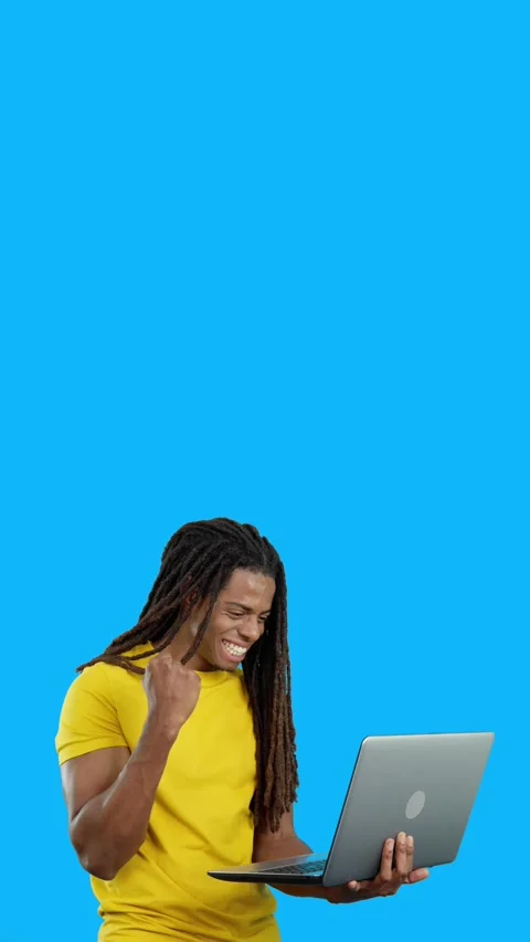 Latin man with dreadlocks celebrating while looking at the laptop Stock Footage 253868962