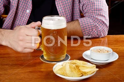Latin man drinking beer and eating snacks at a bar Stock Photos