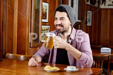 Latin man drinking beer and eating snacks at a bar Stock Photos
