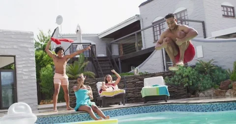 Latin man jumping into swimming pool and laughing with friends at pool party Stock Footage 341466713