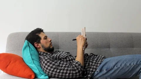 A latin man lying on a couch solving crosswords puzzles in a peaceful attitude 库存影片 340583387