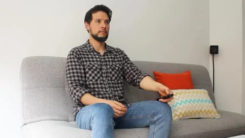 A latin man sitting on a couch turning on the TV with a remote controller Vídeo Stock 340583384