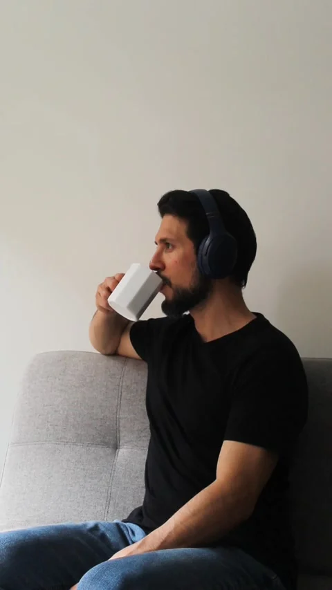 Latin man using headset and drinking something on a white cup Vídeo Stock 340583315