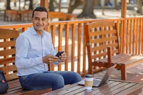 Latin man using a laptop while drinking coffee in a bar outdoors. Photos