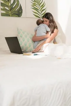 Latin mother using latop while hug side your baby on her bed Stock Photos