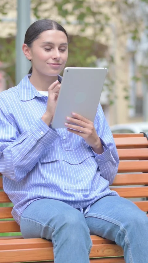 Latin Woman using Tablet while Sitting Outdoor, vertical Video stock 321123757