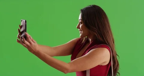 Latina female in sexy red dress taking a selfie on green screen Stock Footage