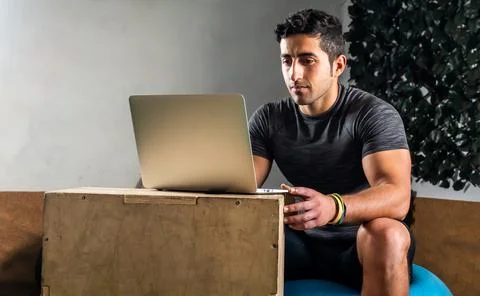 Latino coach working on computer to prepare workout routine in gym Stock Photos