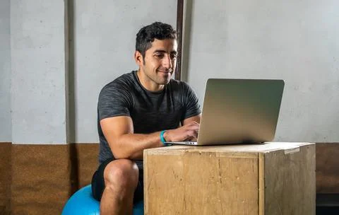 Latino coach working on computer to prepare workout routine in gym Stock Photos