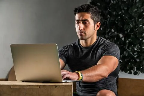 Latino coach working on computer to prepare workout routine in gym Stock Photos