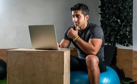Latino coach working on computer to prepare workout routine in gym Stock Photos