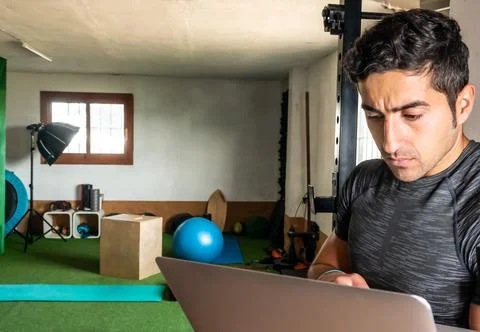 Latino coach working on computer to prepare workout routine in gym Stock Photos