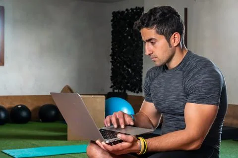 Latino coach working on computer to prepare workout routine in gym Stock Photos