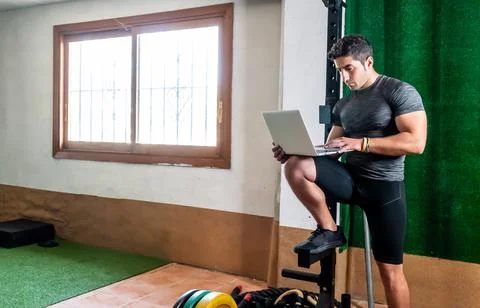 Latino coach working on computer to prepare workout routine in gym Stock Photos