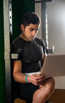 Latino coach working on computer to prepare workout routine in gym Stock Photos