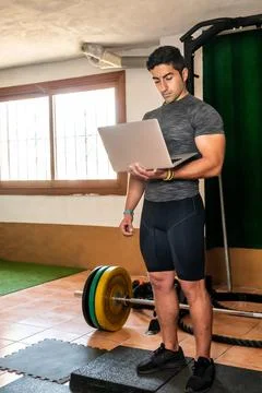Latino coach working on computer to prepare workout routine in gym Stock Photos