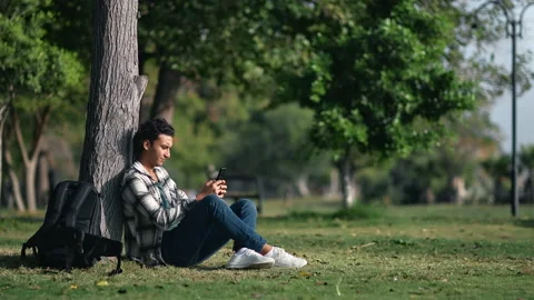 Latino man with backpack enjoy break chatting smartphone relaxing on lawn near Vídeos de archivo 219959839