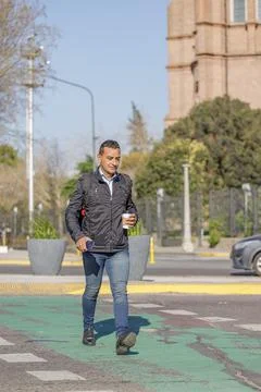 Latino man in jacket and backpack crossing the street in a city. Фото