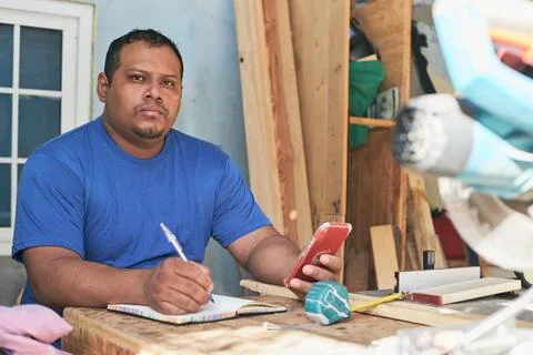 Latino man taking notes of the order, in the cabinetry workshop Stock Photos
