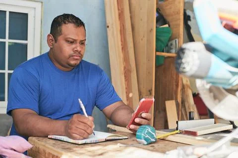 Latino man taking notes of the order, in the cabinetry workshop Stock Photos
