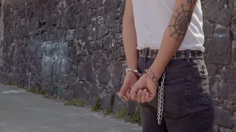 Latino tattooed adult arrested in the street with handcuffs on in the daylight Stock Footage