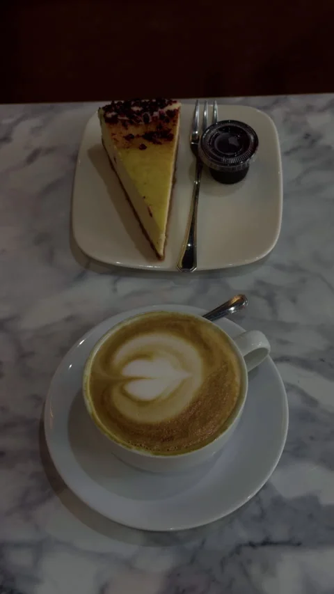 Latte and cheesecake served on marble table in calm cafe setting with top down Stock Footage 344966190
