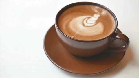 Latte art coffee in brown cup ready for drink on white table at cafe. Vídeo Stock 334648700