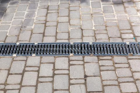 A lattice of a drainage paving system on a path made of square stone tiles. Stock Photos