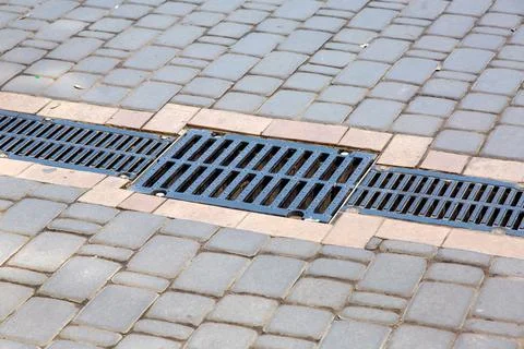 A lattice of a drainage paving system on a path made of square stone tiles. Stock Photos