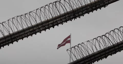 Latvian flag framed by barbed wire coils under a grey sky. Stock Footage 320170491