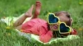 Laughable little girl in big glasses lies on the grass HD Footage