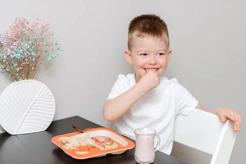 Laughing boy eats delicious pasta at the table in the kitchen Stock Photos