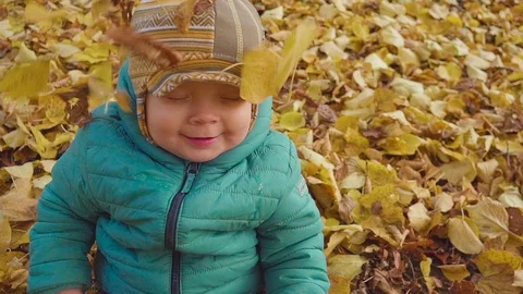 Laughing boy playing with falling leaves in park. slow motion Видео 88665192