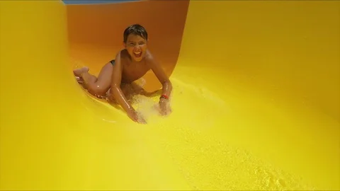 Laughing boy rides down orange slide in a water park Stock Footage 129116987