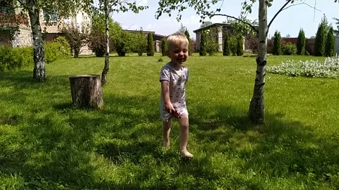 Laughing boy in slow motion running barefoot along the grass between birches Stock Footage 133275629