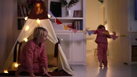 Laughing brothers having fun running and playing in a teepee tent in the evening Stock Footage 130450002
