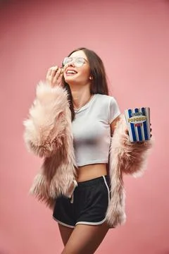 Laughing brunette girl in faux pink fur holding popcorn in hand. Wearing in Stock Photos