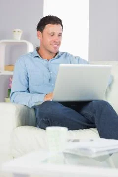 Laughing casual man sitting on couch using laptop Stock Photos