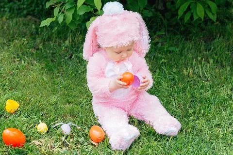 Laughing child at Easter egg hunt baby in pink bunny costume Stock Photos