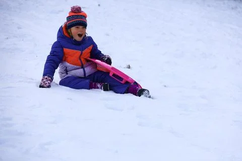 Laughing child falling while sledding on snowy hill during winter playtime Stock Photos