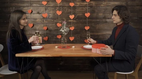 Laughing couple clinking glasses, exchanging valentine presents and kissing Vídeo Stock 124705883