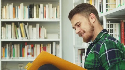 A laughing guy is sitting in the library and reading Video stock 81928773
